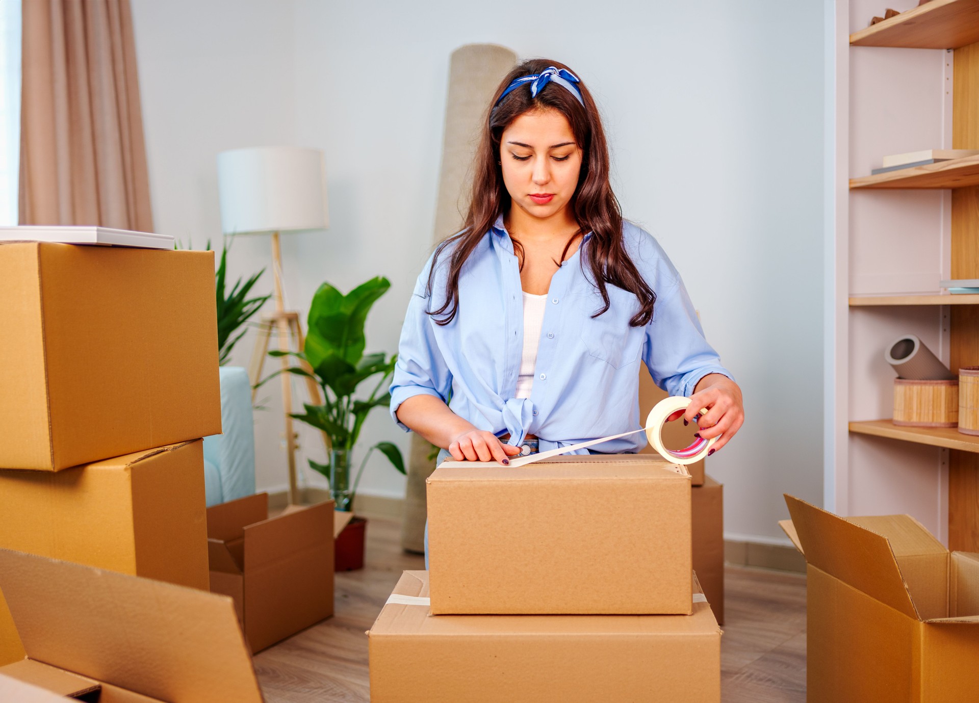Young woman  uses adhesive tape to packing cardboard box. Moving home concept